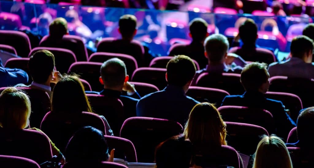 Photo from behind of a darkened auditorium full of people