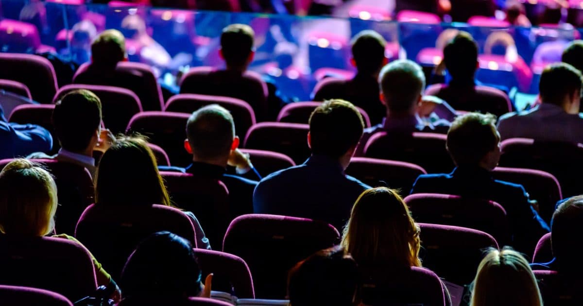 Photo from behind of a darkened auditorium full of people