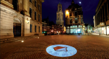 Utrecht stadshuis in het donker met een projectie van het schild van Utrecht op de grond en uitzicht op de Domtoren