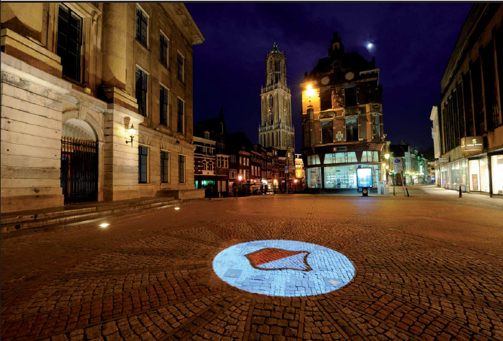 Utrecht stadshuis in het donker met een projectie van het schild van Utrecht op de grond en uitzicht op de Domtoren